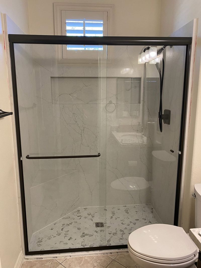 Ducha con paneles tipo mármol, marco negro, banco y mosaico hexagonal