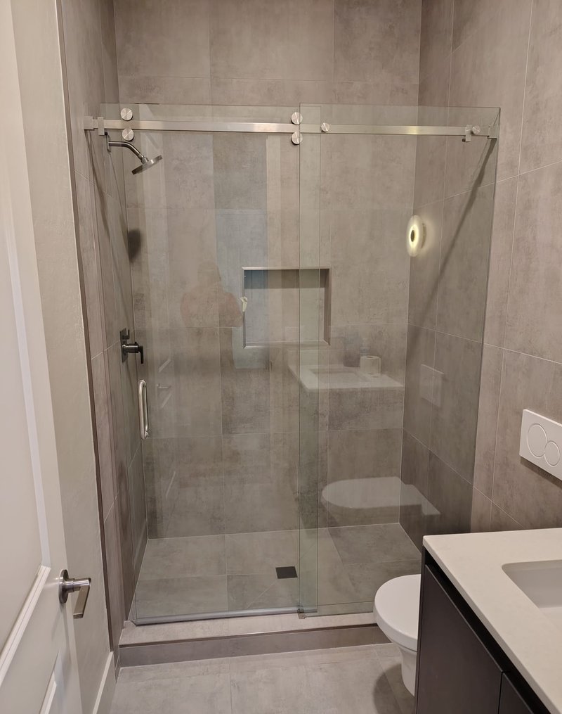 Ducha de porcelanato gris de formato grande con puerta de vidrio corrediza sin marco