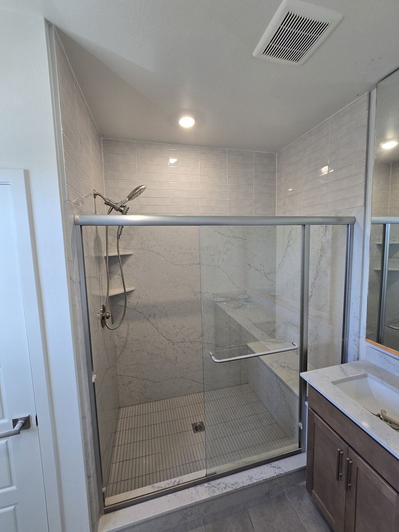 Ducha walk-in con paneles tipo mármol, banco y puerta de vidrio
