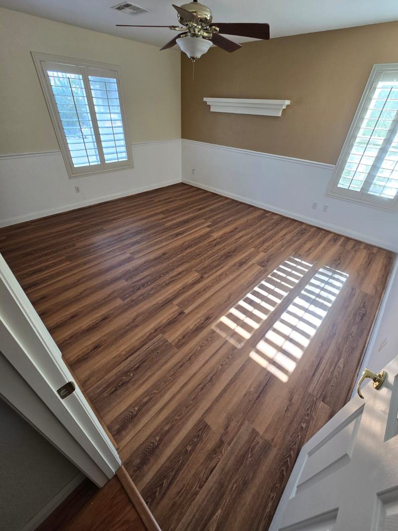 Piso SPC tono madera instalado en habitación con wainscoting blanco