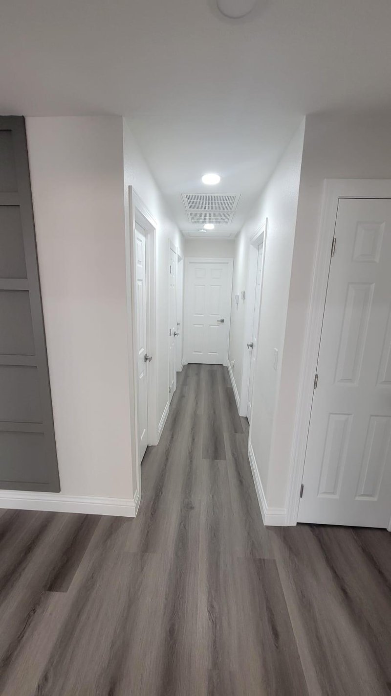 Pasillo con piso vinílico LVP gris recién instalado y baseboards blancos